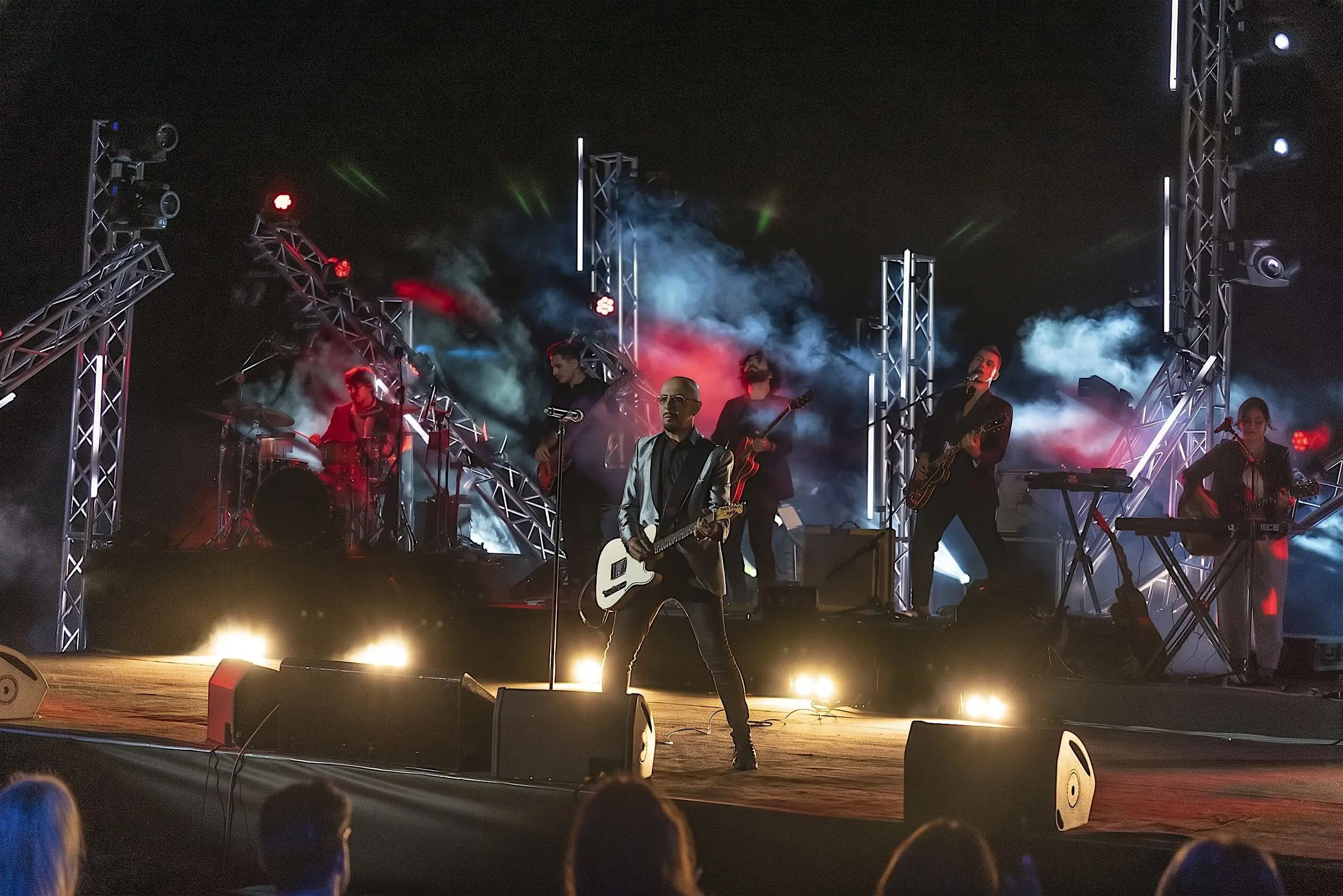Band playing on a stage with trusses, haze and lights
